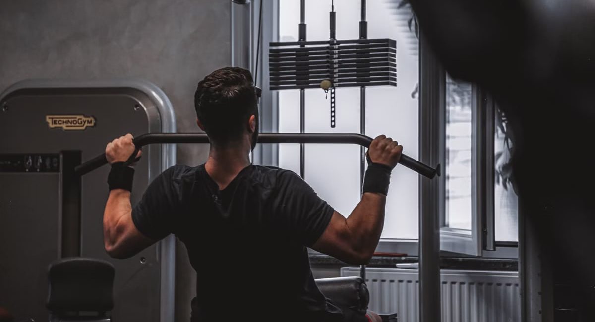 Back view of a man exercising with lat pulldown machine in the gym.